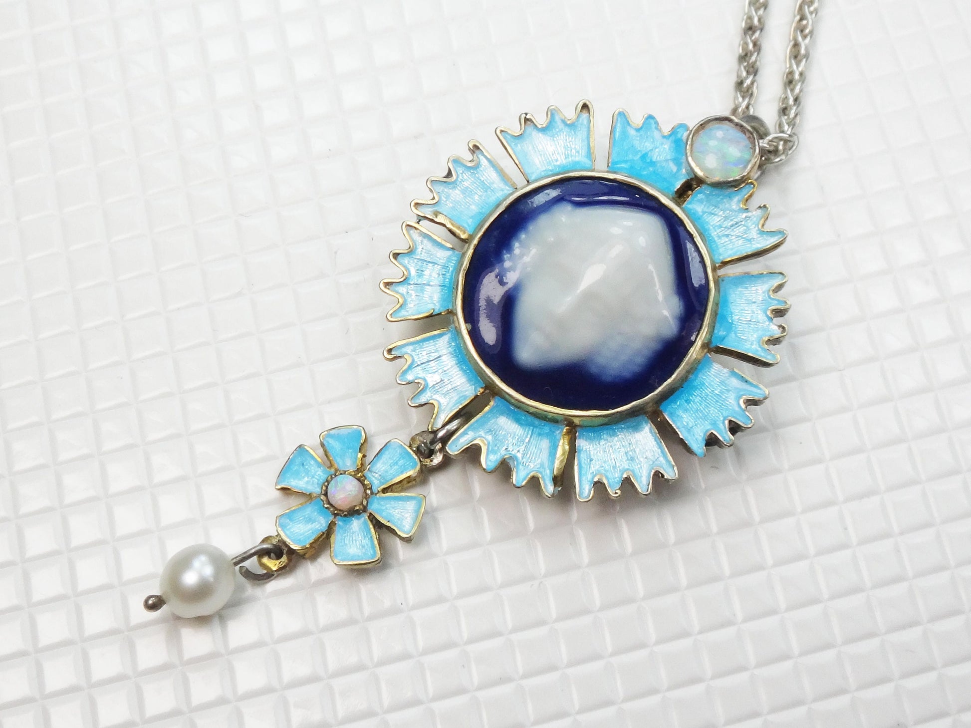 Vintage Sterling Silver Blue Limoges Porcelain Cameo Necklace and Earrings with Bacchus Design.  In this photo is a silver pendant necklace of Limoges porcelain and blue and white enamel flower design. The pendant has an opal at the top and white pearl hanging from the bottom. The necklace is on a silver chain.