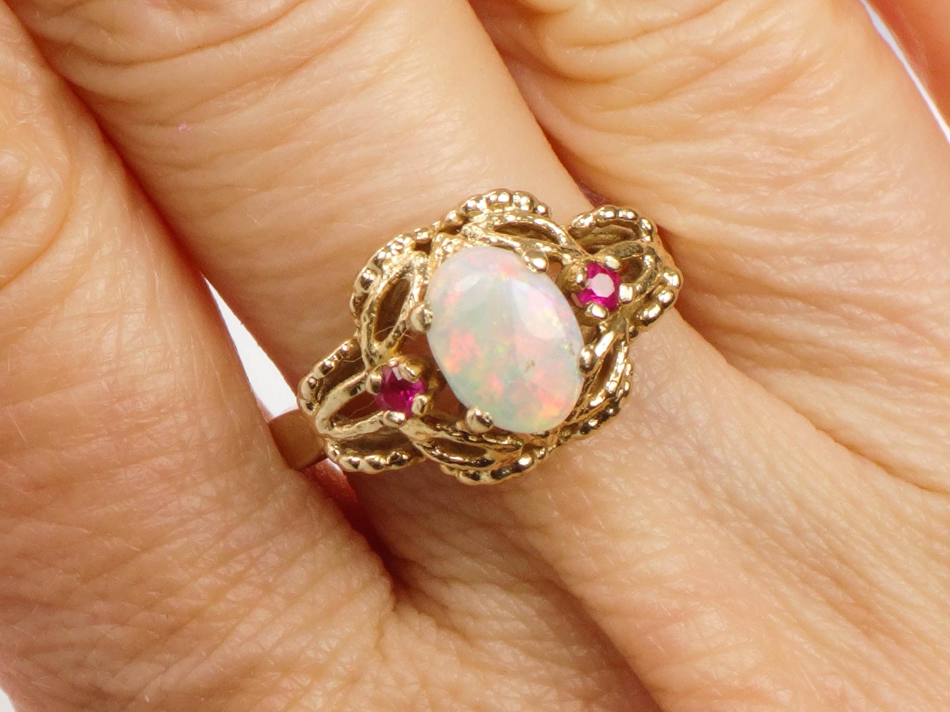 Vintage 14k Yellow Gold Genuine Opal Ring with Rubies October Birthstone Size 6.25, A gold ring with an oval shaped opal gemstone and two ruby accents. The ring has a delicate, intricate design.