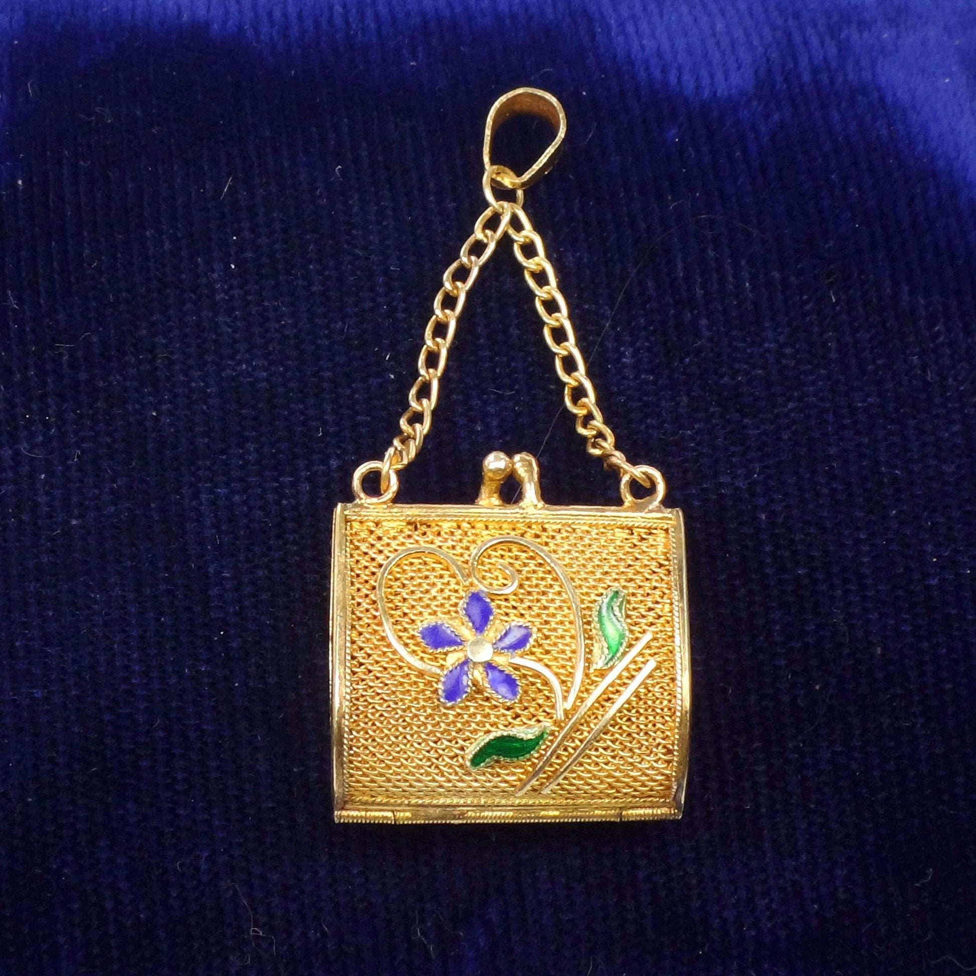 A Vintage Gilt Silver pendant in the shape of a small purse with a chain. The purse has a blue flower with green leaves on the front and the pendant has moving parts.