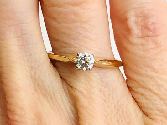 May include: A solitaire diamond engagement ring with a round-cut diamond. The diamond is set in a four-prong setting on a delicate yellow gold band. The ring is simple and elegant, perfect for a classic engagement ring.